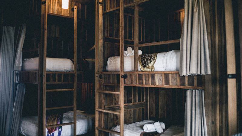 2 bunk beds side by side with a modern looking timber frame, white curtain on each bed, and white sheets
