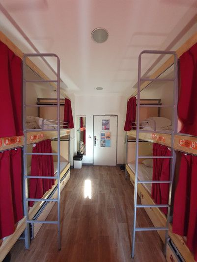 4 bunk beds with ladders leading up to each top bunk, red curtains over each bed