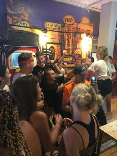 Multiple young people partying and doing karaoke while other take pictures in a bar setting
